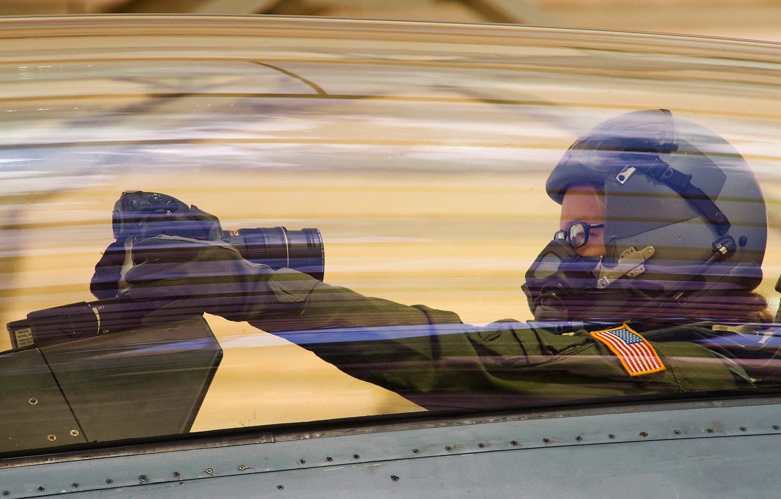 Air Force photojournalist in a flight helmet photographing from a fighter jet cockpit. View the original photo on af.mil.