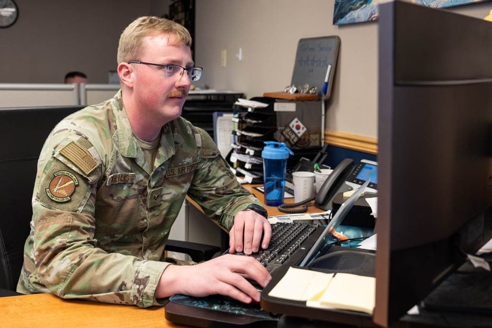 Air Force finance specialist reviewing financial records at a computer workstation